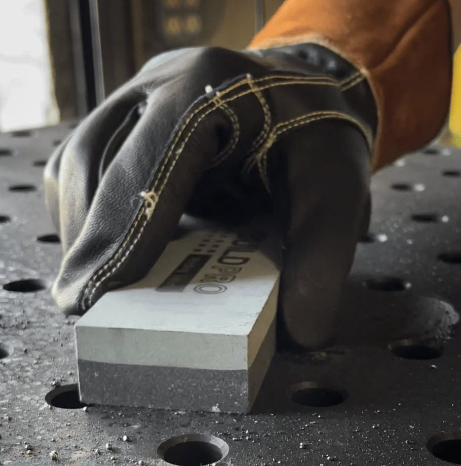 Gloved hand holding a BuildPro sharpening stone on a welding table