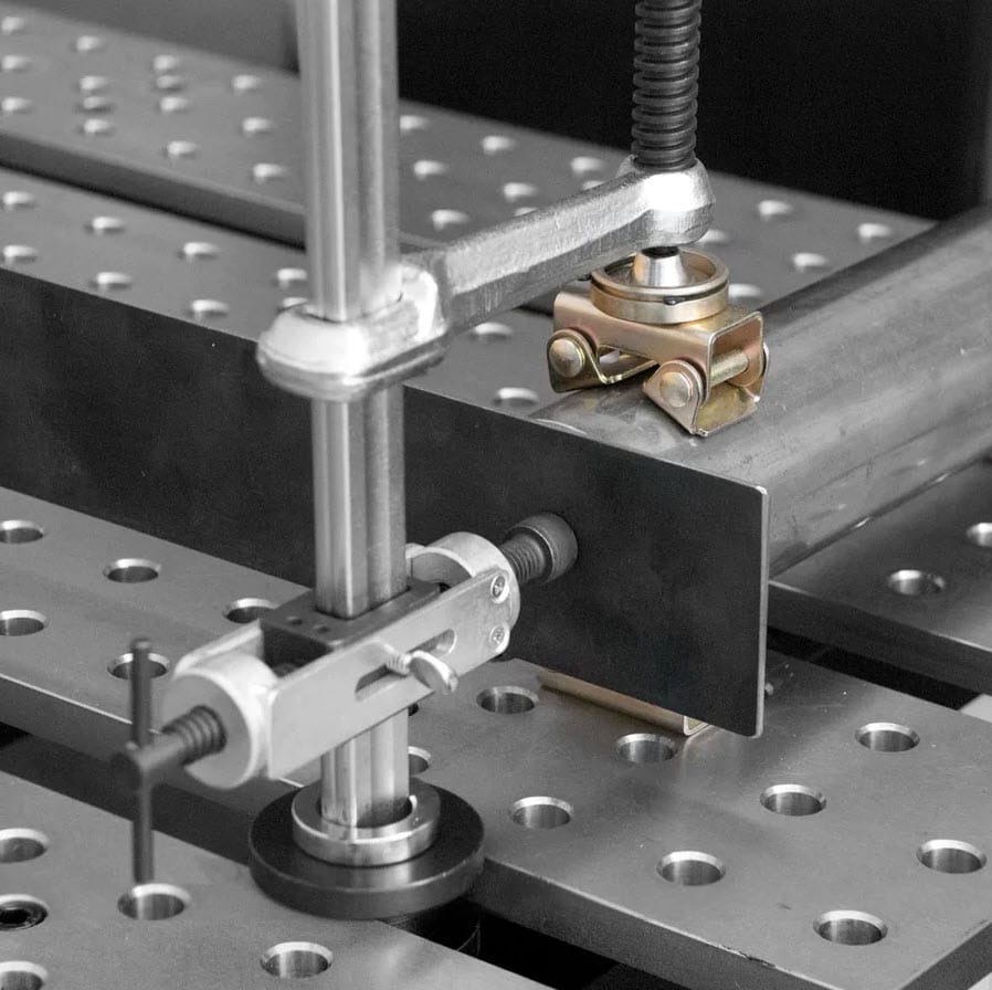 BuildPro welding clamp securing metal pipe to a perforated steel fixture table