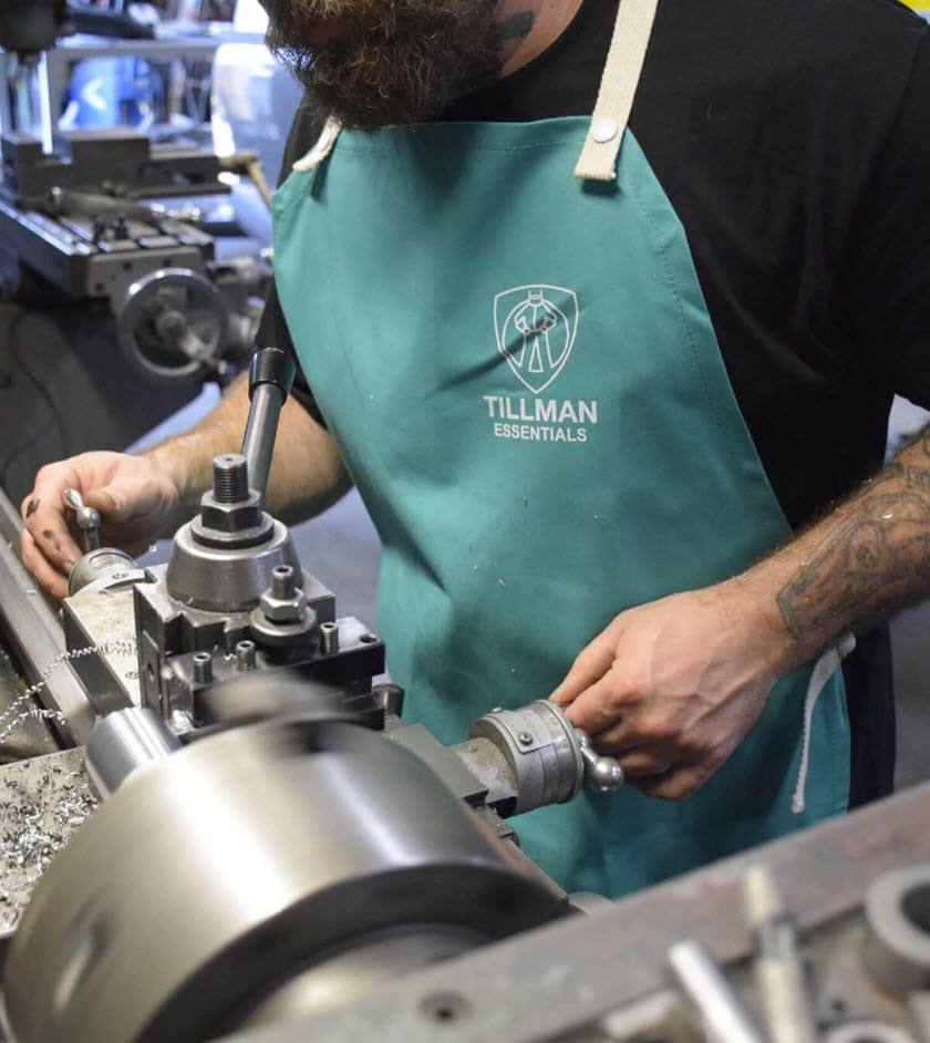 Person wearing a green Tillman Essentials apron operating a metal lathe