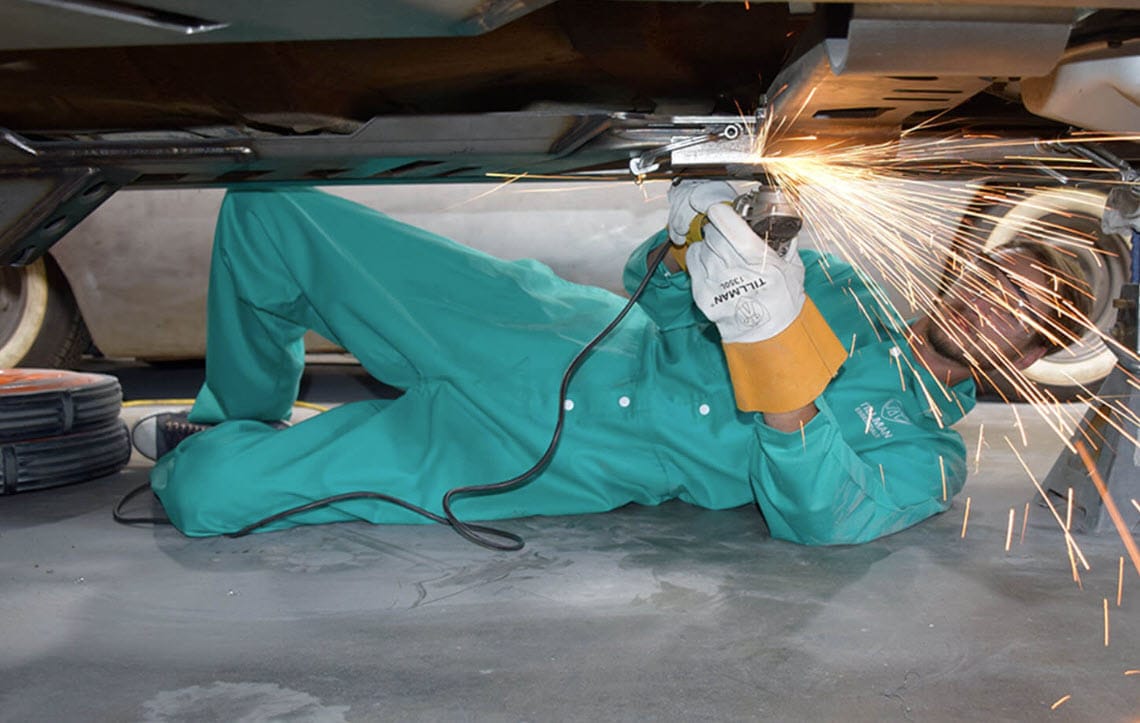 Worker wearing Tillman gloves using a grinder on a vehicle undercarriage