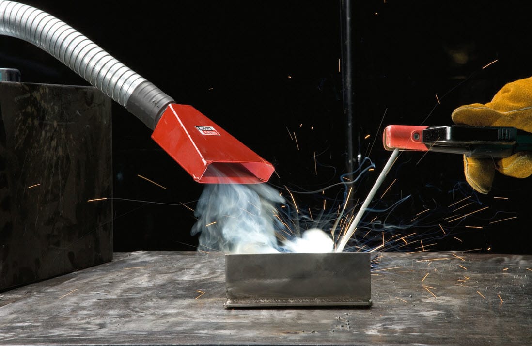 Welding torch with fume extraction nozzle capturing smoke and sparks on a metal workbench