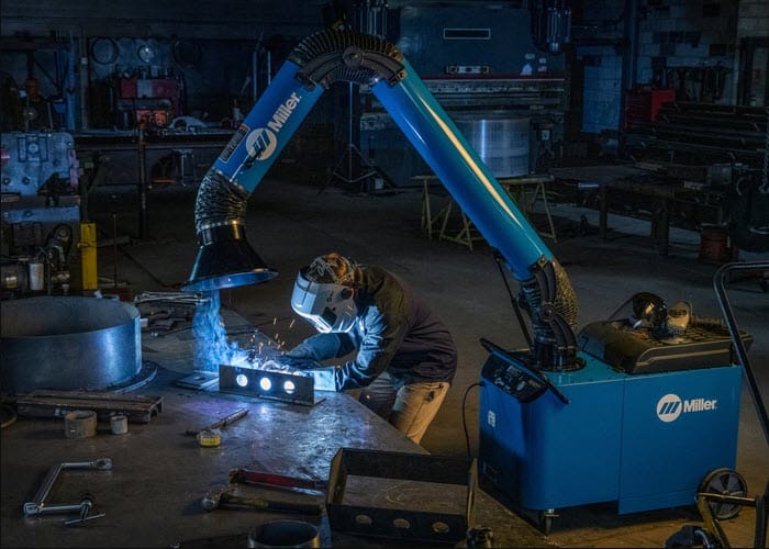 Welder wearing protective gear using a Miller fume extraction system in a workshop