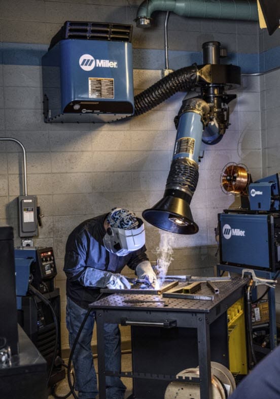 Welder wearing protective gear working at a table with a Miller fume extraction system