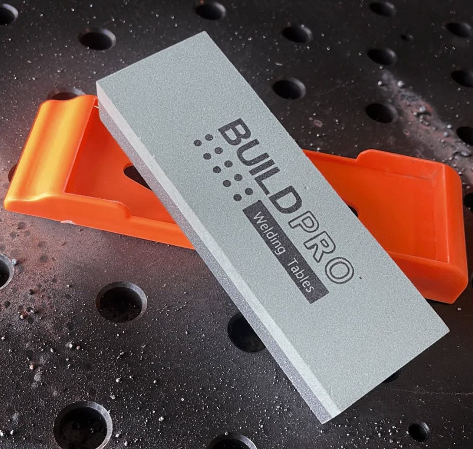 BuildPro abrasive cleaning stone on an orange holder resting on a welding table