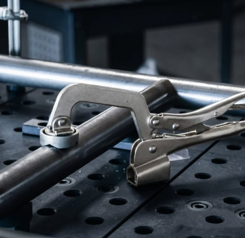 BuildPro locking C-clamp securing a metal pipe to a welding table