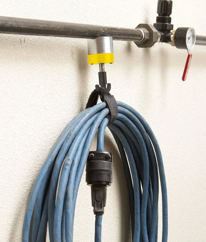 Magswitch magnetic hook holding a coiled blue extension cord on a metal pipe