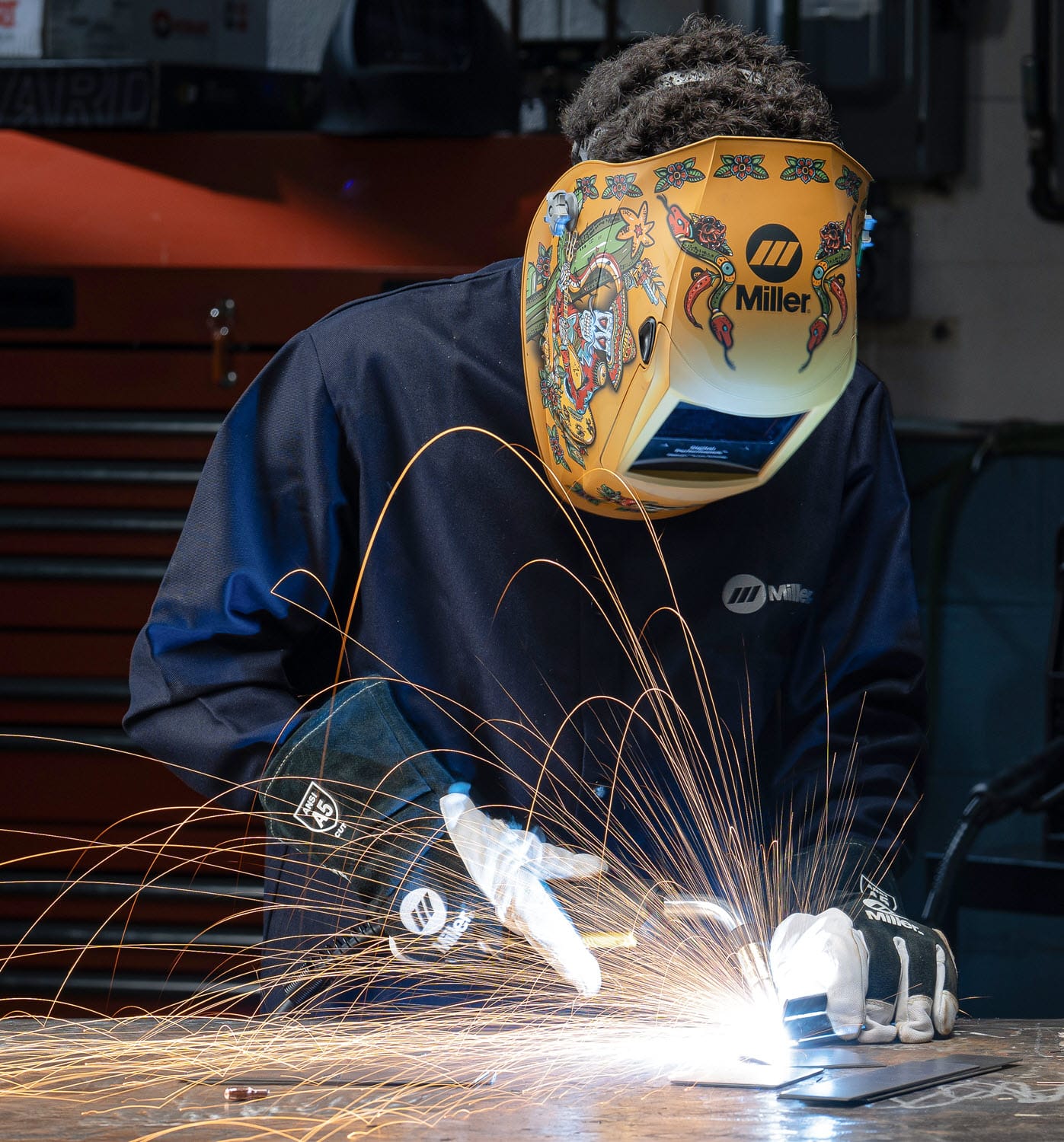 Welder wearing a Miller helmet and protective gloves working on metal with sparks flying